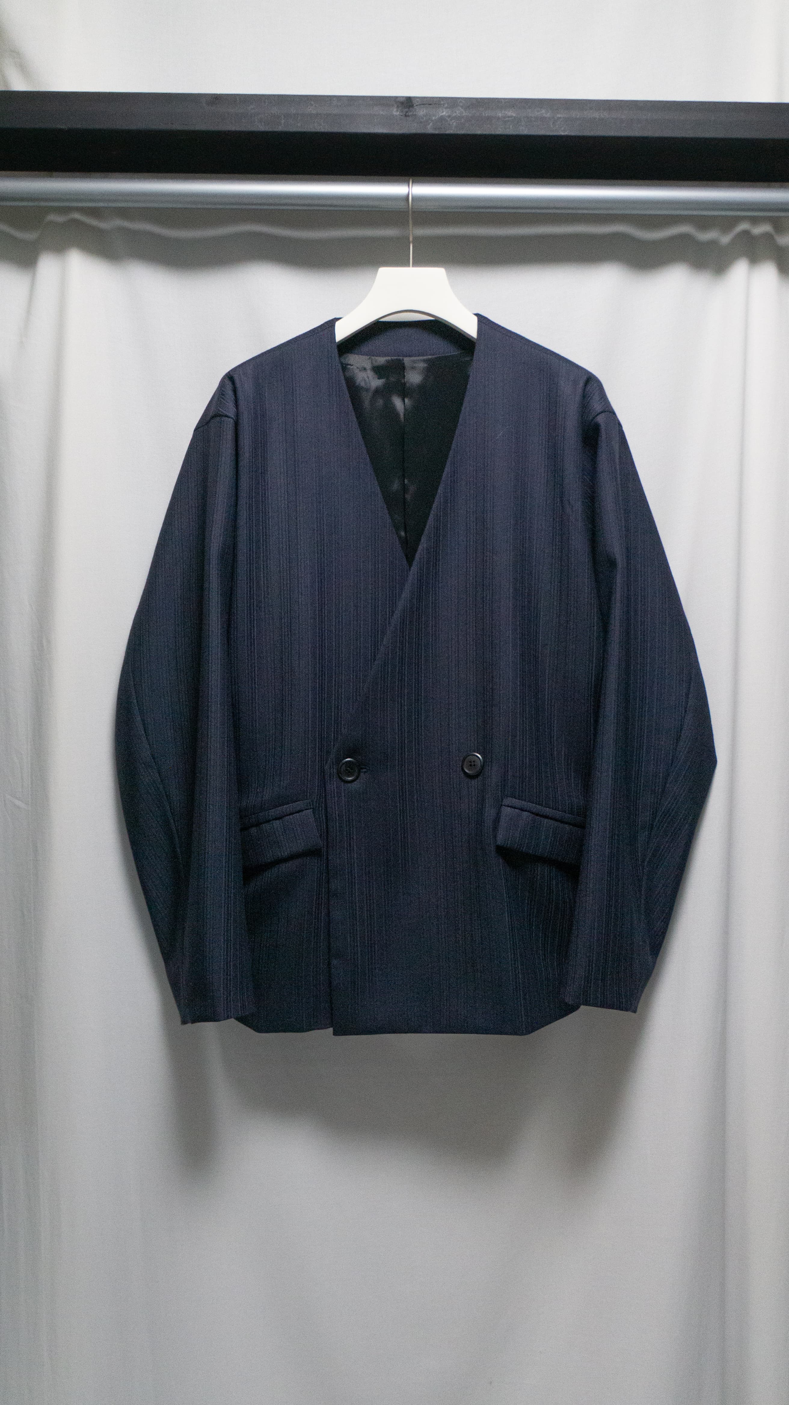 中肉の光沢感の強いダブルクロスを使用した一着。太めの両玉縁ポケットとフラップで個性を出しつつノーカラーで落ち着いた印象に。